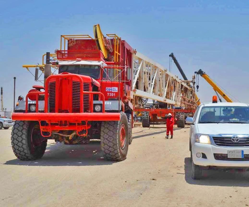 Red oilfield truck carrying a rig mast section beside a support vehicle